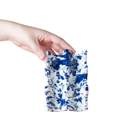 Hand holding a blue and white patterned ceramic item against a pink background