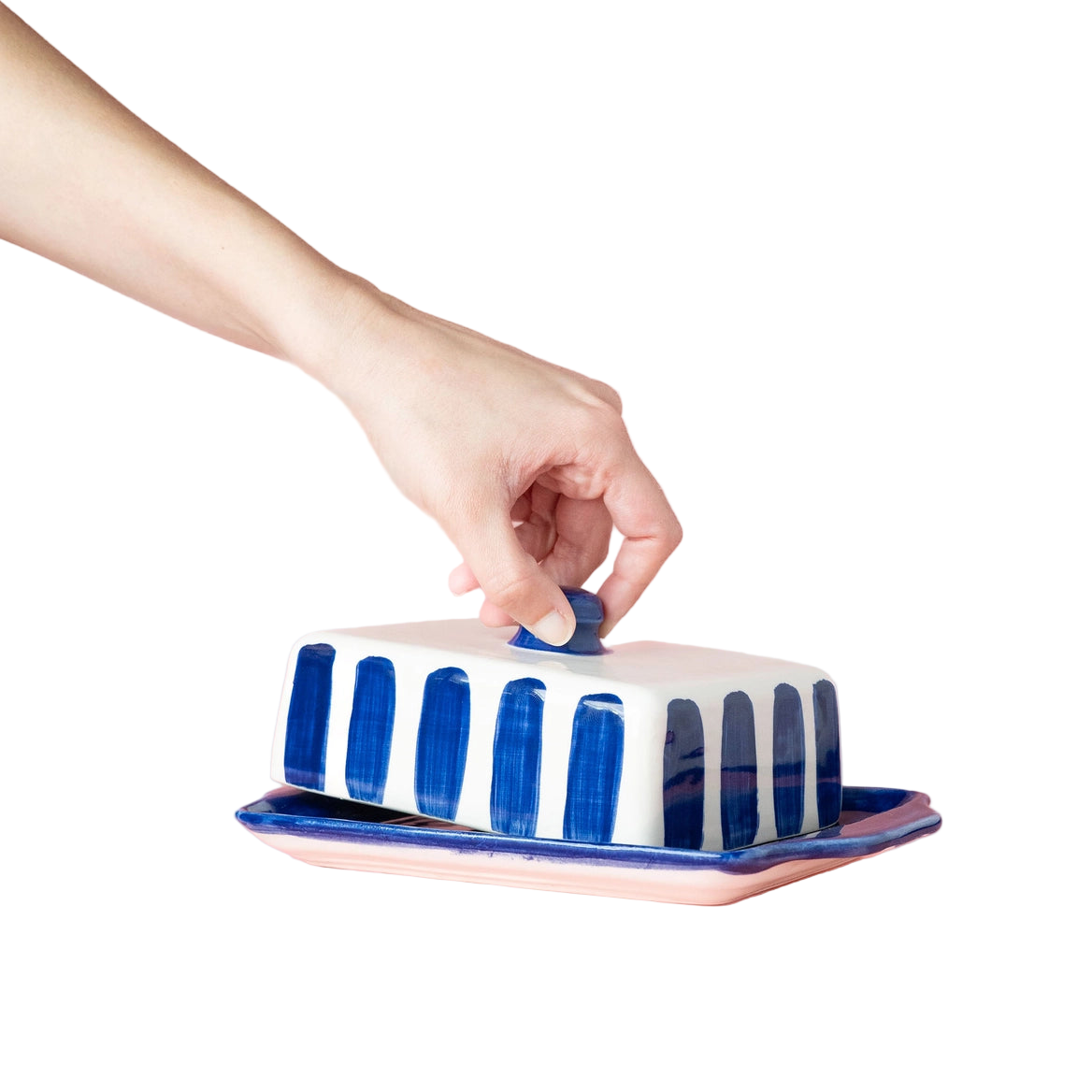 Hand closing a blue and white striped butter dish on a pink background