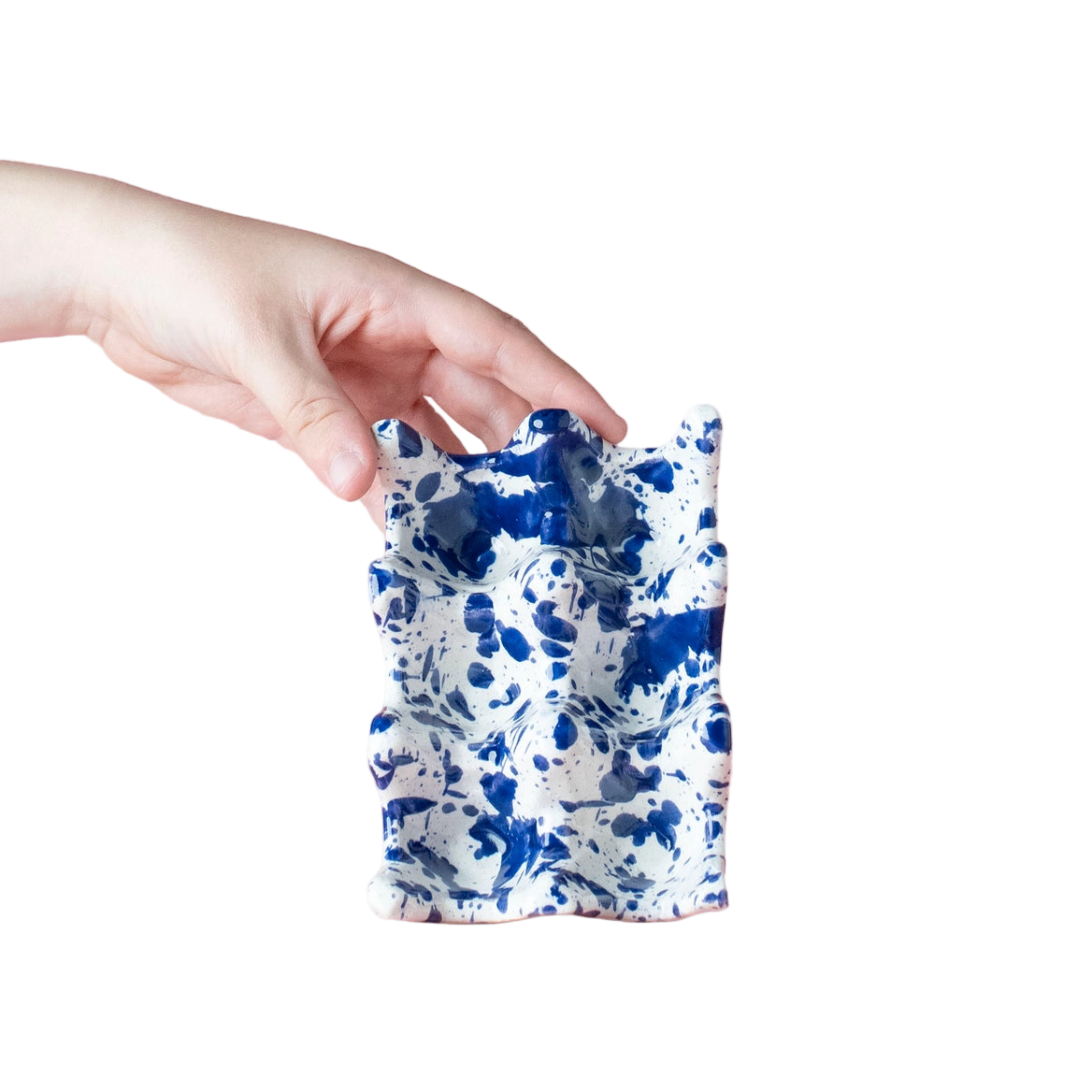 Hand holding a blue and white patterned ceramic item against a pink background