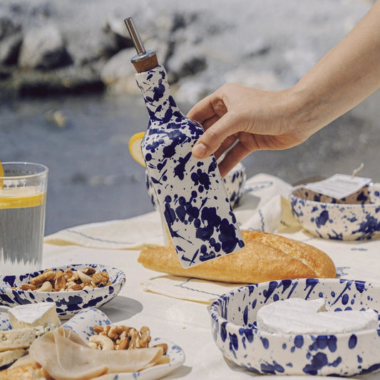 Hand reaching for a floral-patterned bottle cap on a table with food and drinks by the sea.